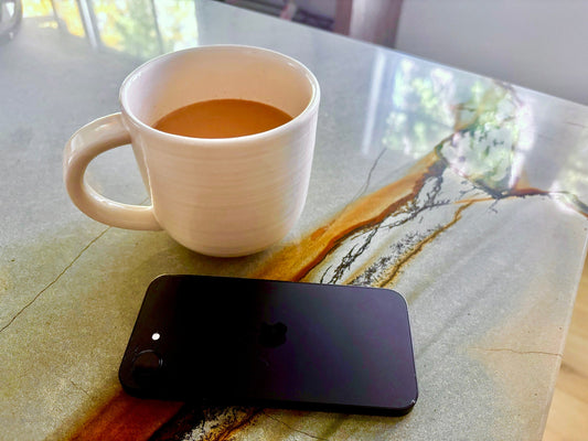 Cup of coffee in a white mug with black cell phone face down on a marble counter in a Lake Minnetonka home.