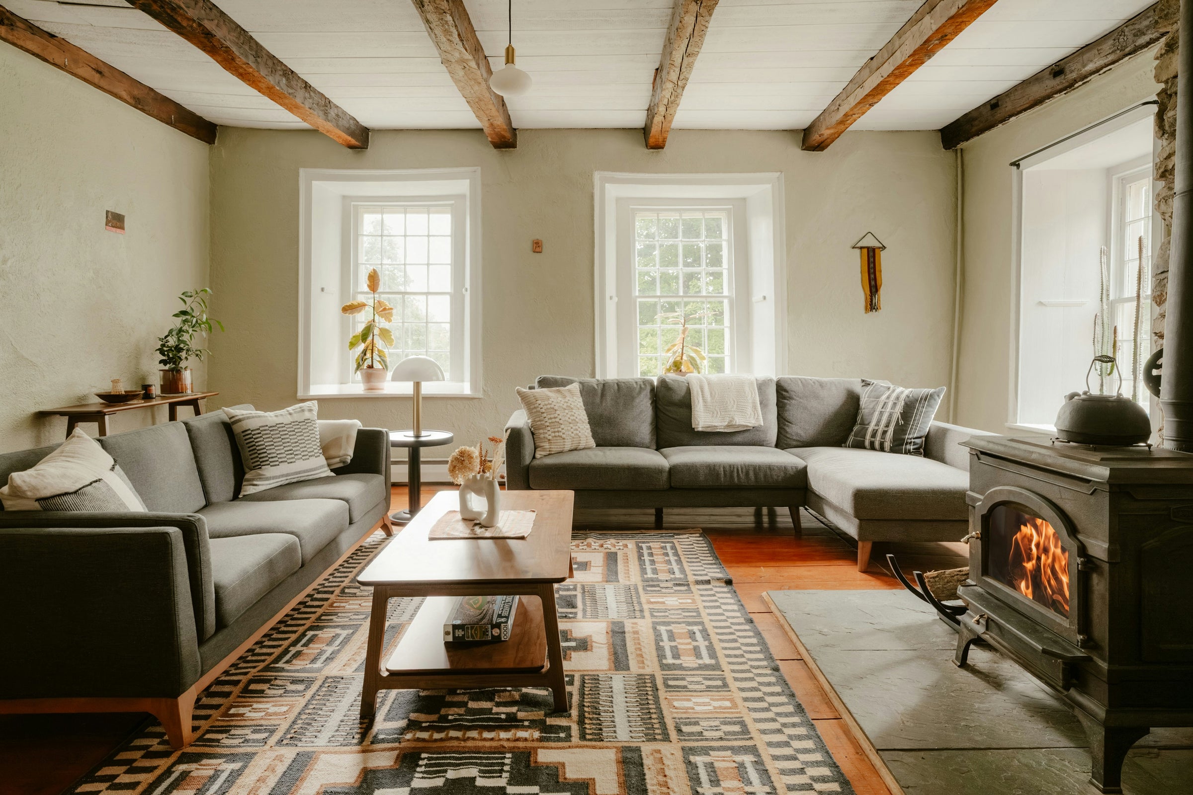 A living room with exposed wood ceiling beams and a fireplace, lit by daylight.
