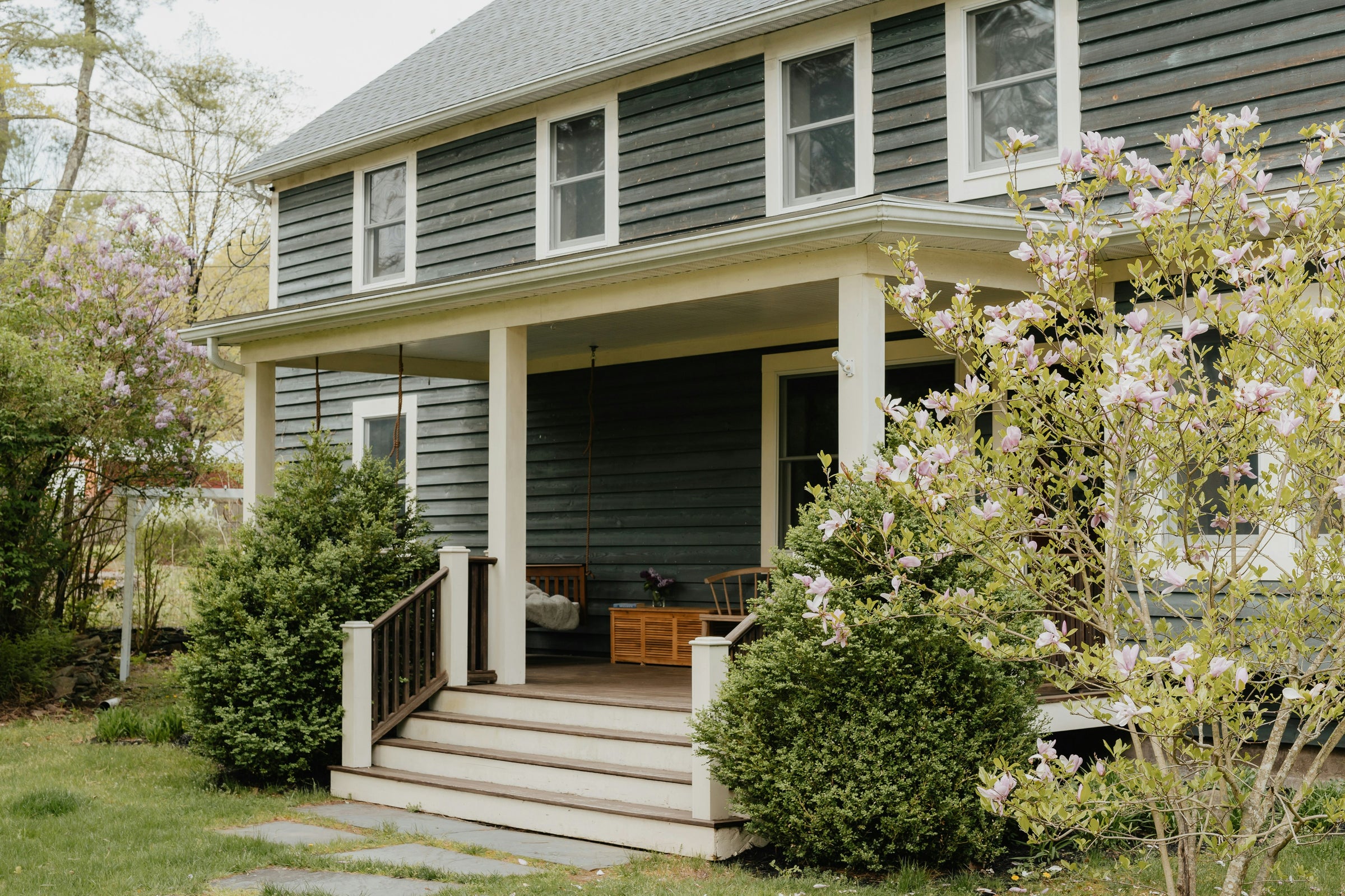 A front porch with a swing and wide steps, framed by a blooming magnolia.